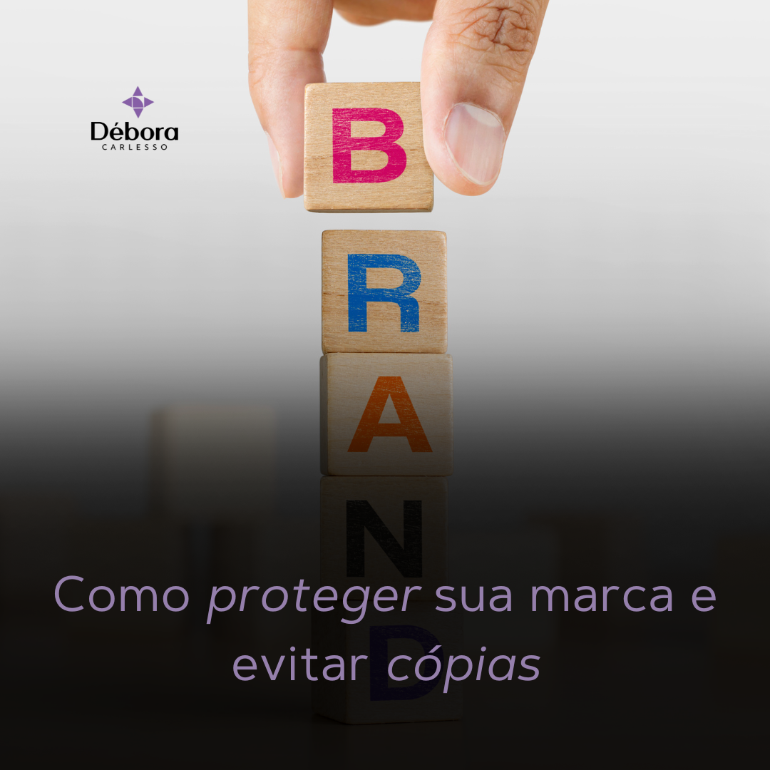 Imagem com a palavra "BRAND" formada por blocos de madeira empilhados. No topo, uma mão segura o bloco com a letra B. Na parte inferior da imagem, está escrito: "Como proteger sua marca e evitar cópias", junto ao logotipo da Débora Carlesso Advocacia.
